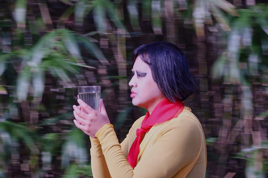 Video still of artist holding glass cup in front of bamboo | Photo courtesy Anthony Le
